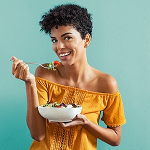 Woman in yellow shirt smiling while eating healthy meal