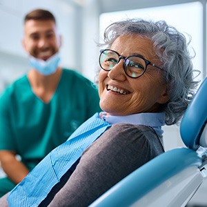 Woman with glasses smiling while sitting in treatment chair