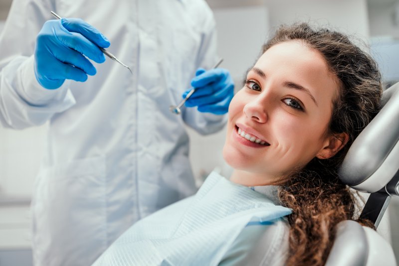 A woman sitting in a dental chair while smiling at a dentist